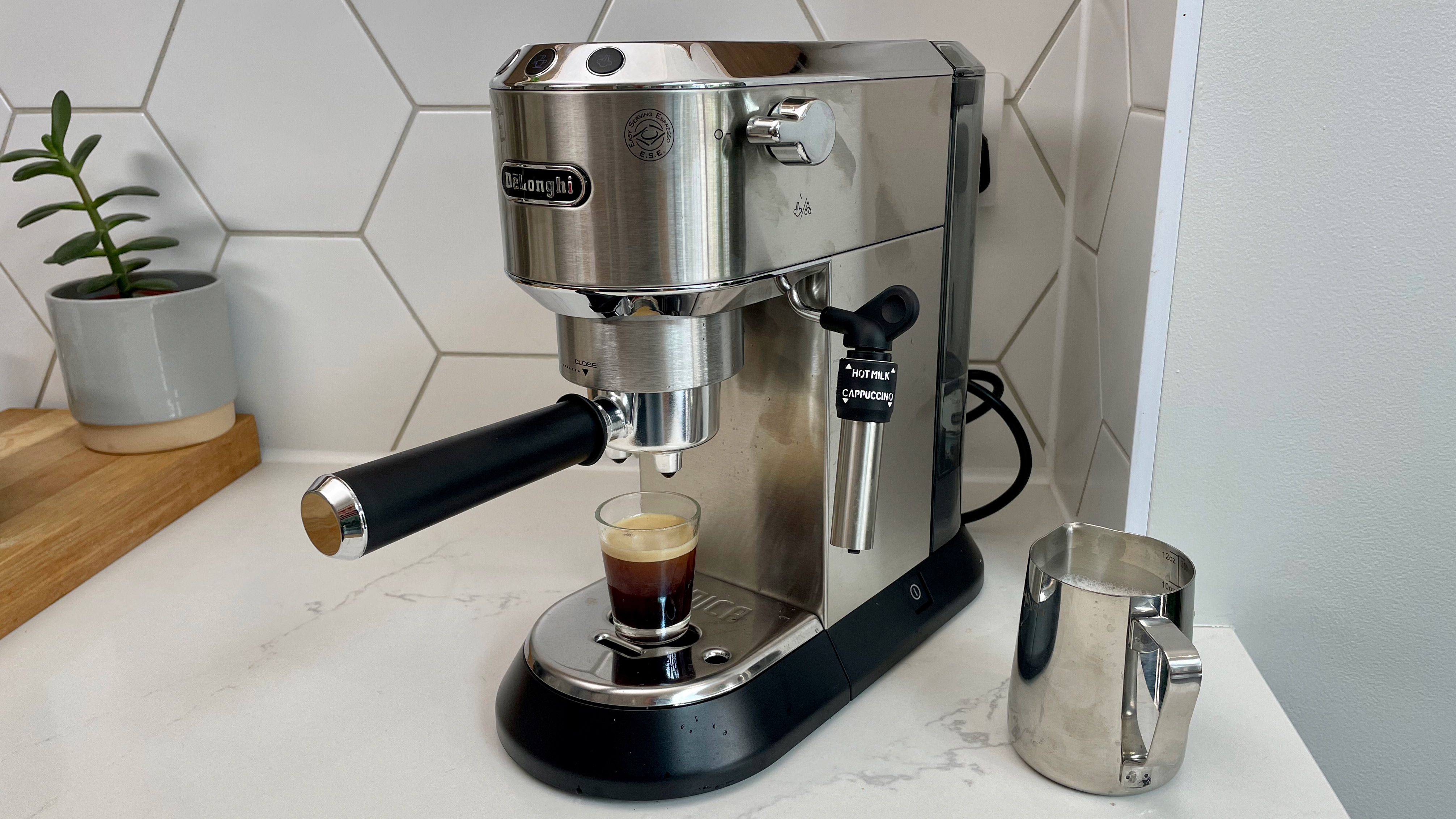 En DeLonghi Dedica Style EC685 står på en vit köksbänk och har precis bryggt en espresso.