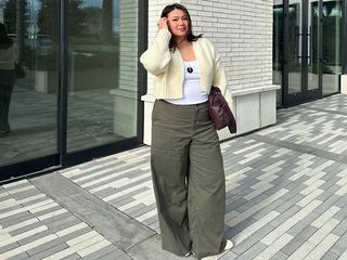 Marina wears olive pants, white shirt, yellow sweater, and brown clutch.