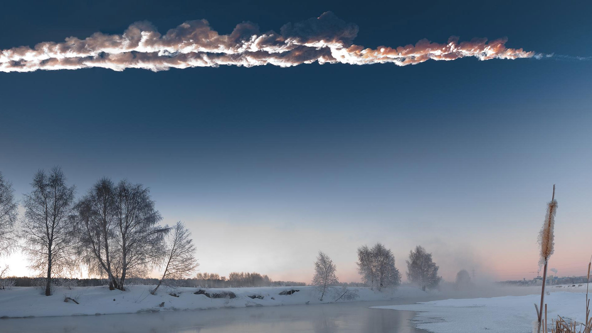 a contrail created by a meteor streaks across a dawn sky above a winter landscape