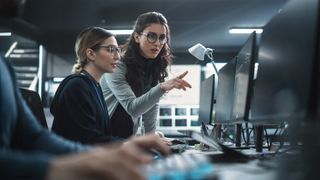 Female CISO advises colleague in a security operations center while working on desktop computers.