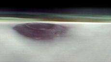 a purple-hued volcano pokes through a thick layer of clouds 