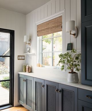 kitchen with navy cabinets with cane inset, tongue and groove paneling and natural blind