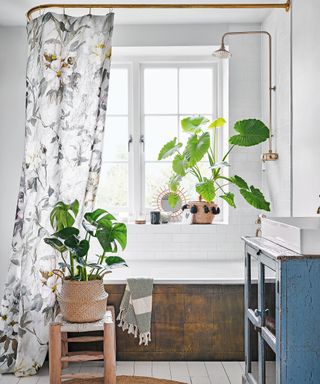 bathroom with wooden floor, patterned shower curtain around bath and plants in woven baskets