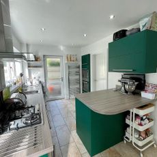 a kitchen with brown tile flooring and brown cupboards with a radiator rail next to inbuilt ovens stacked on top of each other, view showing the back door