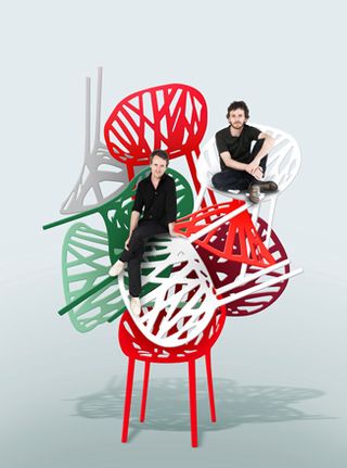 Two men sitting on a stacked pile of colourful big chairs