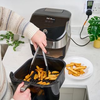 black air fryer drawer with chips inside and tongs placing chips on white plate