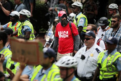 A white supremacist rally participant surrounded by police officers.
