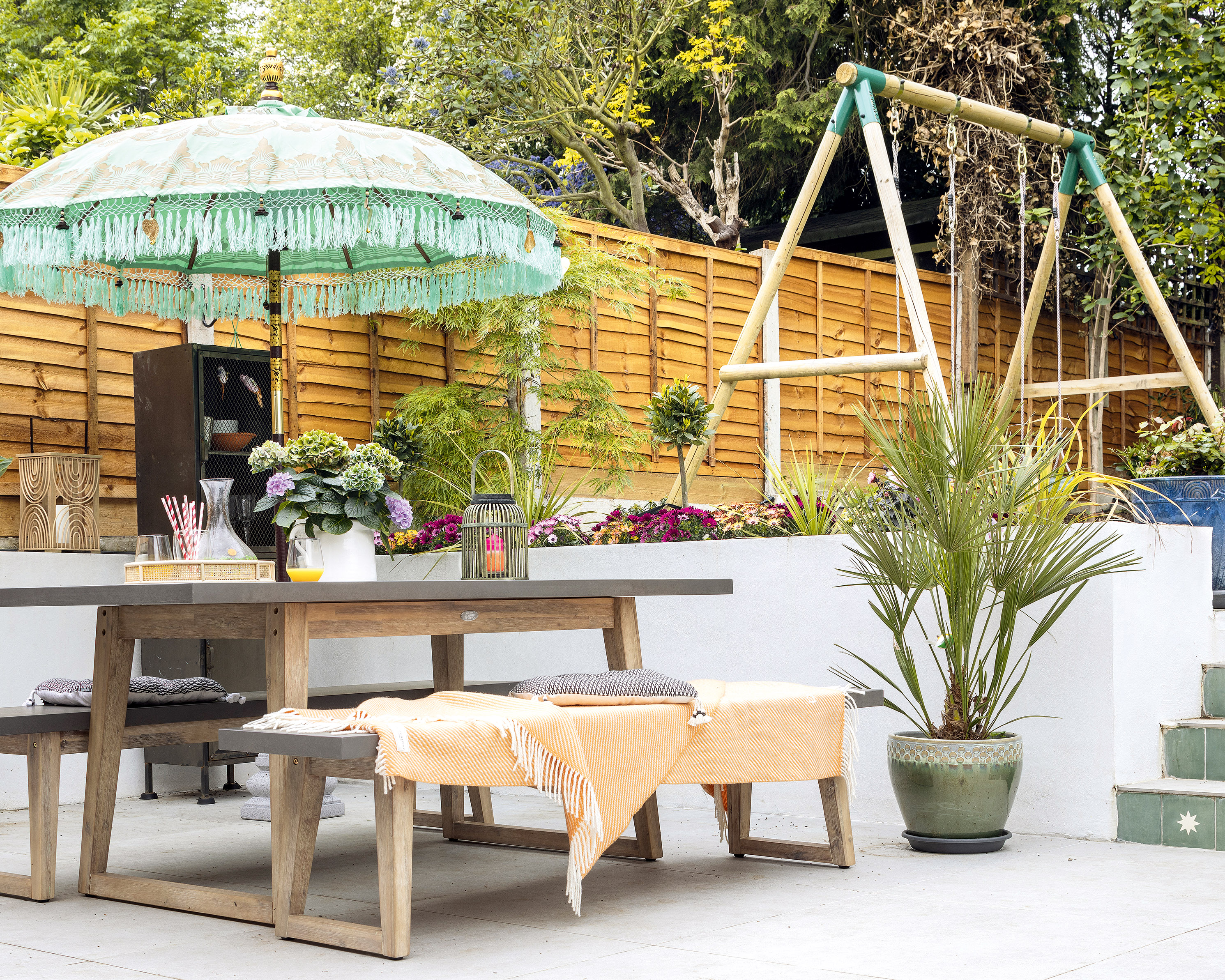 modern split level garden with dining bench set, turquoise parasol and kids swing