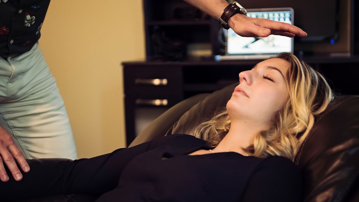 young woman with dyed blonde hair lying down, relaxed with her eyes closed, as a man holds a man about a foot over her face