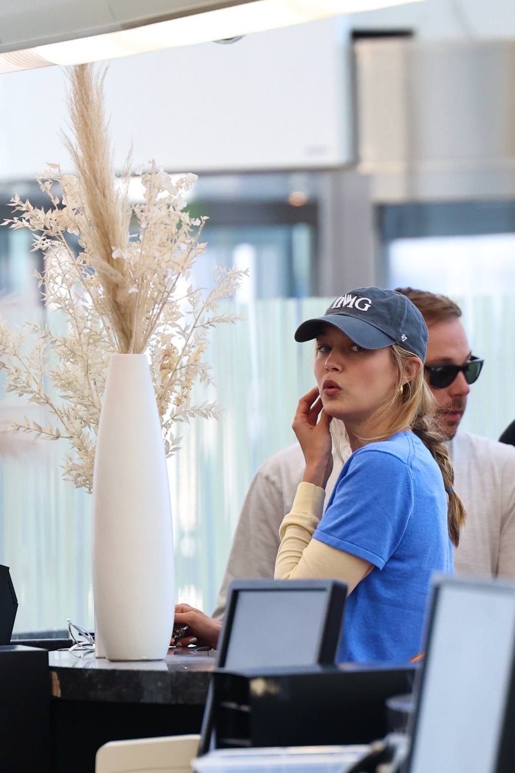 Gigi Hadid no aeroporto vestindo uma camiseta azul, calça branca, mocassins amarelos e um boné de beisebol preto