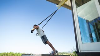 A man uses the TRX Home2 System suspension trainer outside his house on a sunny day to work his upper body