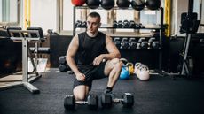 A man in the gym standing next to a pair of dumbbells