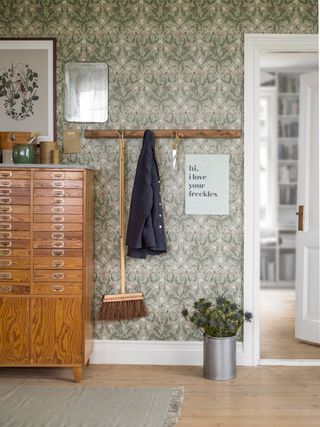 floral wallpaper in hallway with coat rack and drawers