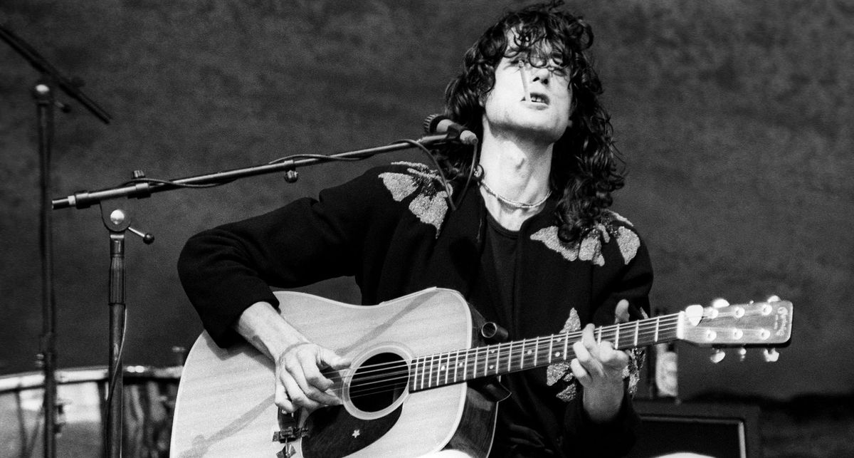 A black and white photo of Jimmy Page playing a Martin D-18 onstage, cigarette in his mouth