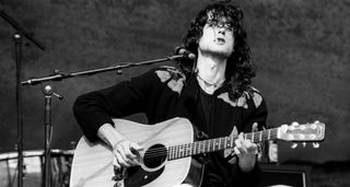 A black and white photo of Jimmy Page playing a Martin D-18 onstage, cigarette in his mouth