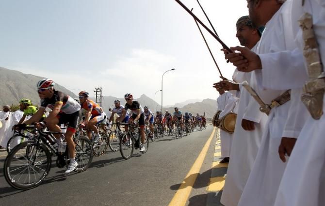 Cyclists racing in the Wadi al-Awabi area, west of Muscat, pass by Omani nationals performing their traditional dance during the third stage of Tour of Oman