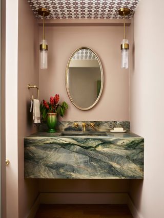 Bathroom with wall-to-wall green marble vanity, oval mirror, brass ceiling lights and tiled ceiling