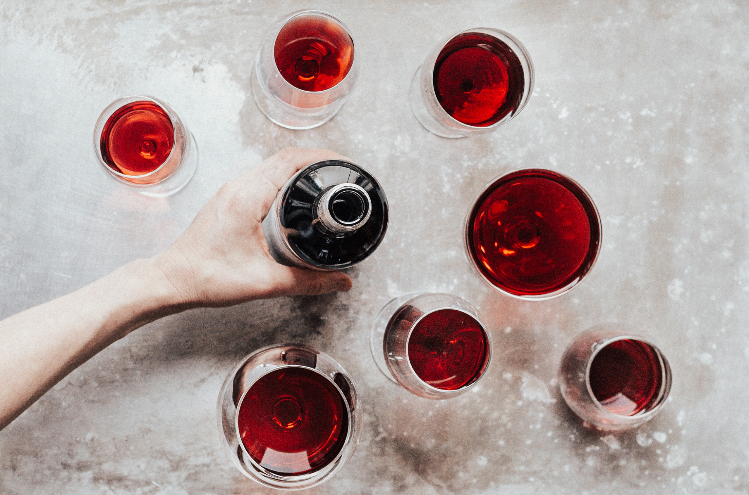 A birds eye shot of several glasses of red wine, different sized glasses and shades of red