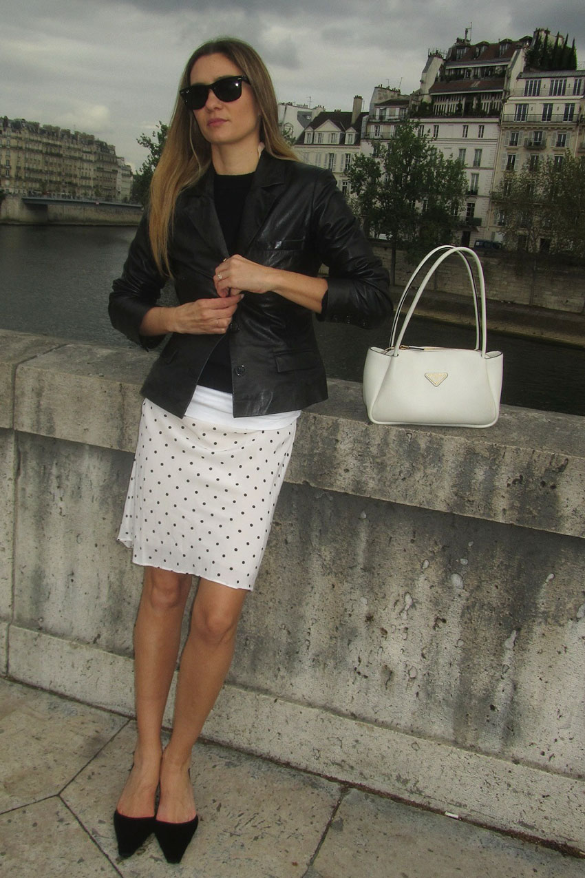 A French woman wearing a black leather blazer, black shirt, and white polka dot skirt with black slingback heels