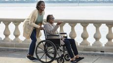 A daughter pushes her mom in a wheelchair while walking across a bridge.