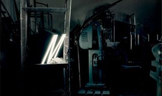 Black and white image of a room with machinery and a light up letter M on a metal shelf