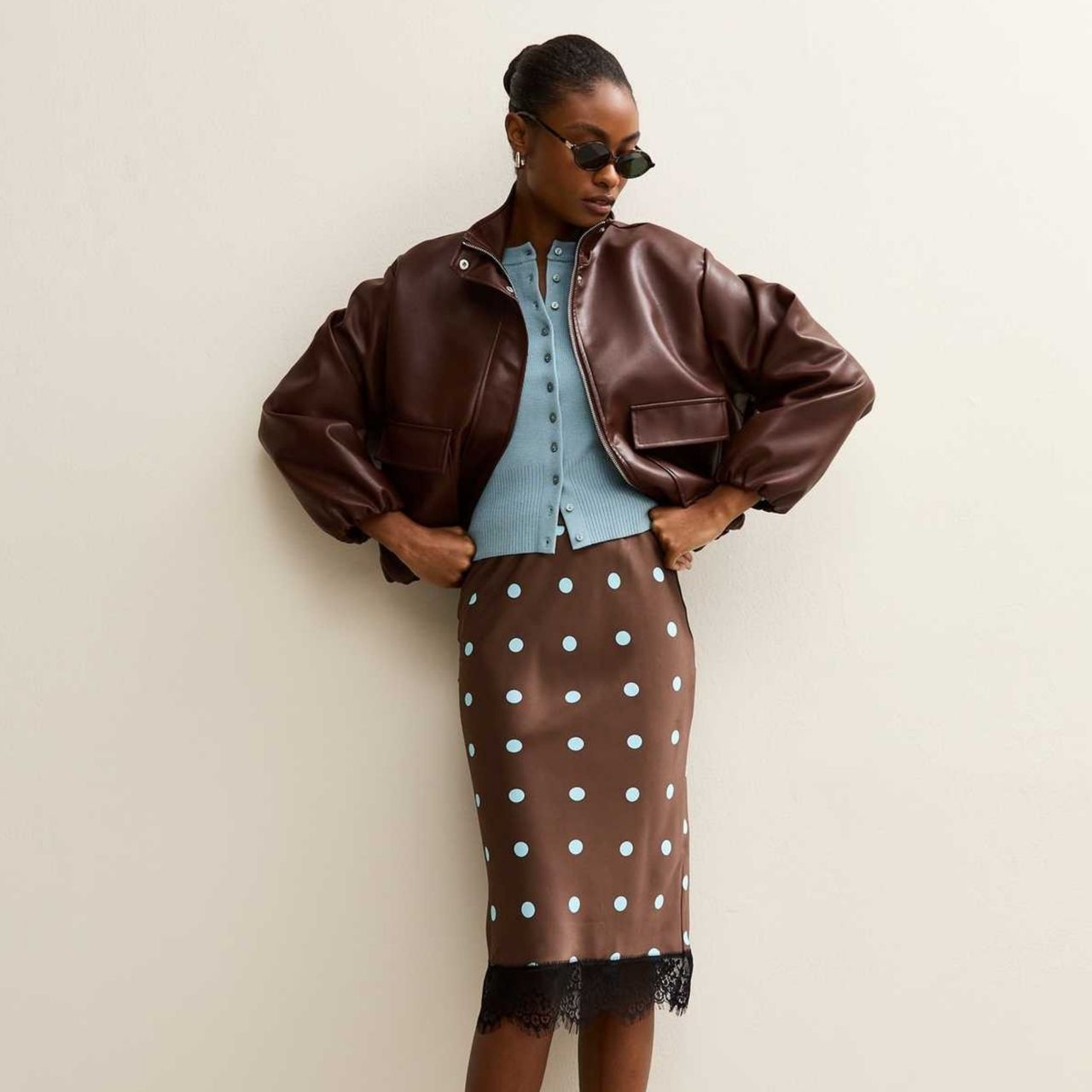 A model wearing a brown bomber jacket, blue cardigan and polka dot skirt from New Look.