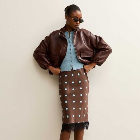 A model wearing a brown bomber jacket, blue cardigan and polka dot skirt from New Look.