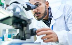 Portrait of young Middle-Eastern scientist looking in microscope while working on medical research in science laboratory, copy space