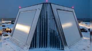 A trapezoidal building with slanted straight sides is covered in snow amidst a snowy landscape.
