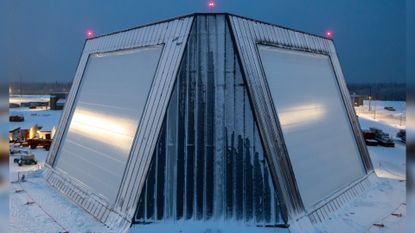 A trapezoidal building with slanted straight sides is covered in snow amidst a snowy landscape. 
