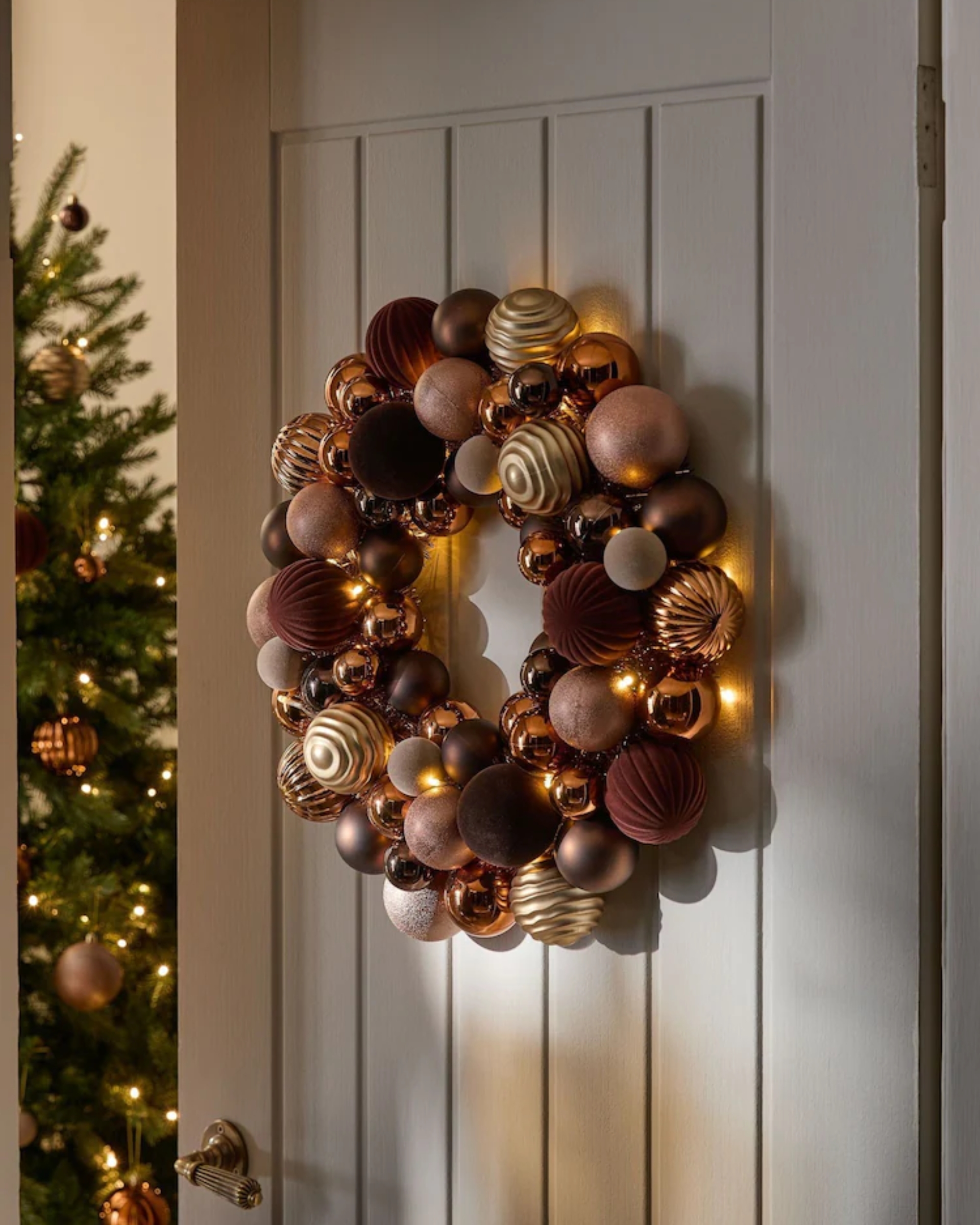 Image of a bauble wreath in a tonal brown colorway hanging on a beige door.