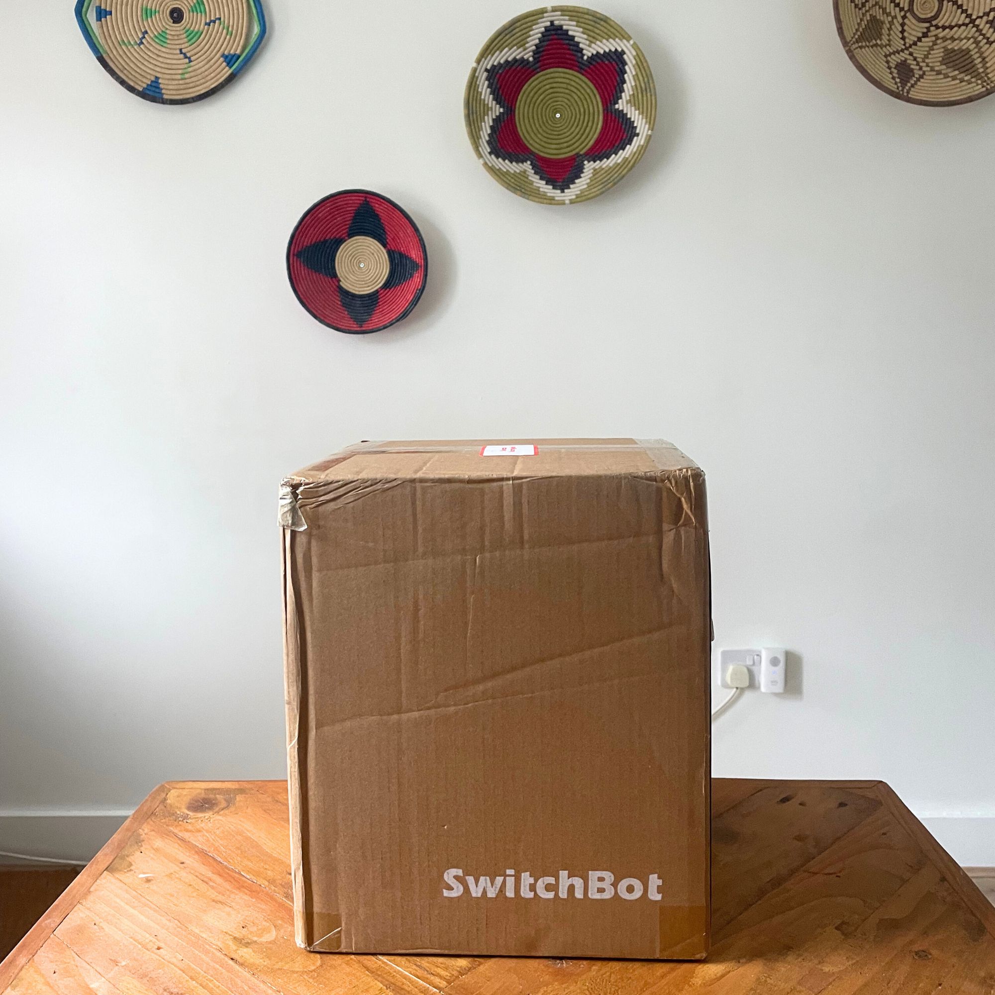 SwitchBot K11+ Robot Vacuum Cleaner with Mop box sitting on a wooden table with a white wall behind it