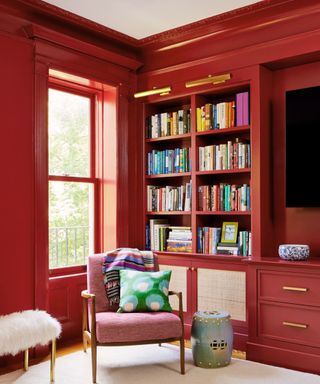 living room with dark red walls, built-in shelving and pink armchair