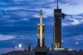 A triple core black and white rocket with used boosters on launch pad with clouds in background