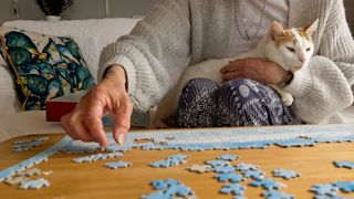 A woman does a puzzle with a cat on her lap