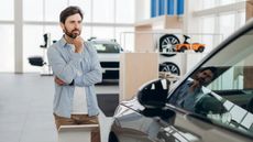 Male customer thinking about buying a new car in a car dealership showroom