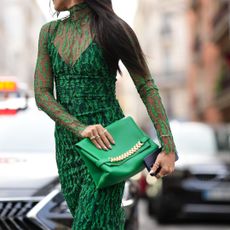 A street style image of a guest at Paris Fashion Week wearing a green lace dress, a green leather clutch bag and winter chrome nails