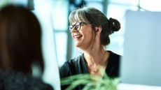 Woman smiling at desk looking at computer screen to highlight menopause in the workplace