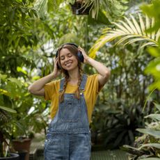 A smiling woman listens to headphones among leaves