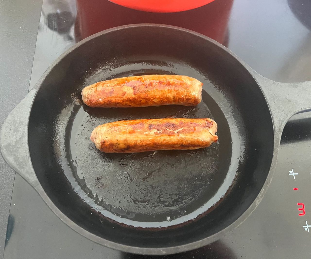 Two golden brown sausages in a small black cast iron skillet