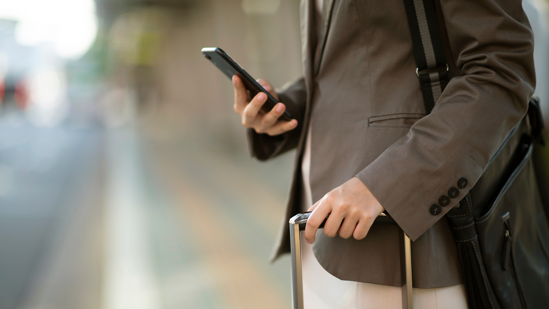 Traveller holding a smartphone and wheeled suitcase