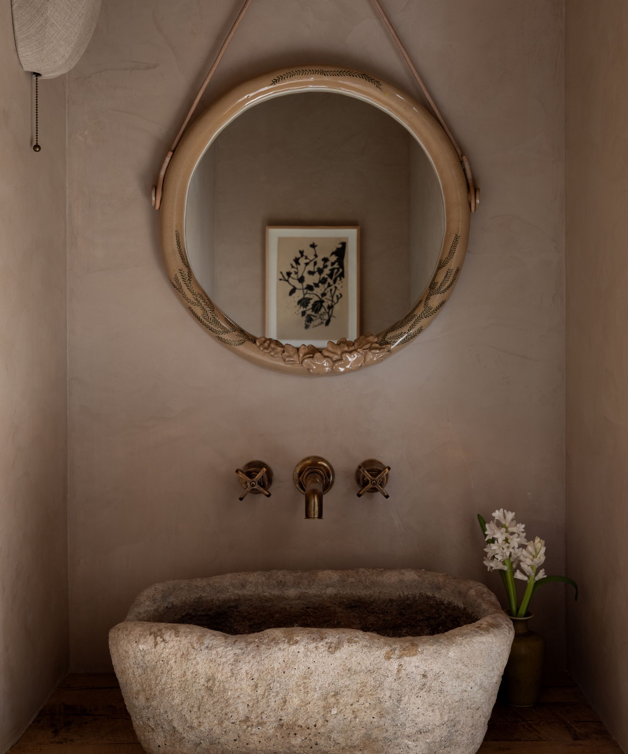 a warm beige plastered powder room with a small stone basin sink and brass wall mirror