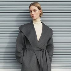 Model wears yellow turtleneck and grey wide collar coat