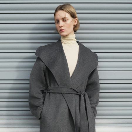 Model wears yellow turtleneck and grey wide collar coat