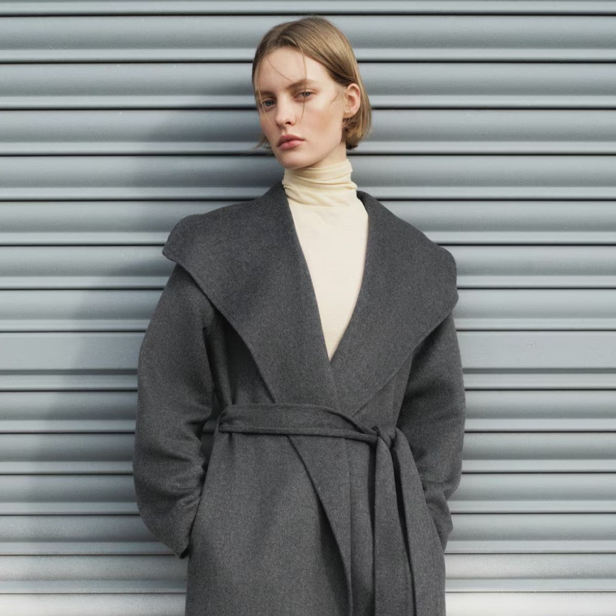 Model wears yellow turtleneck and grey wide collar coat