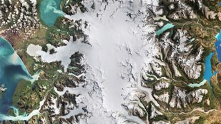 A view of Earth from space, with snow in the middle of the image and a series of green coastlines with water around the snow