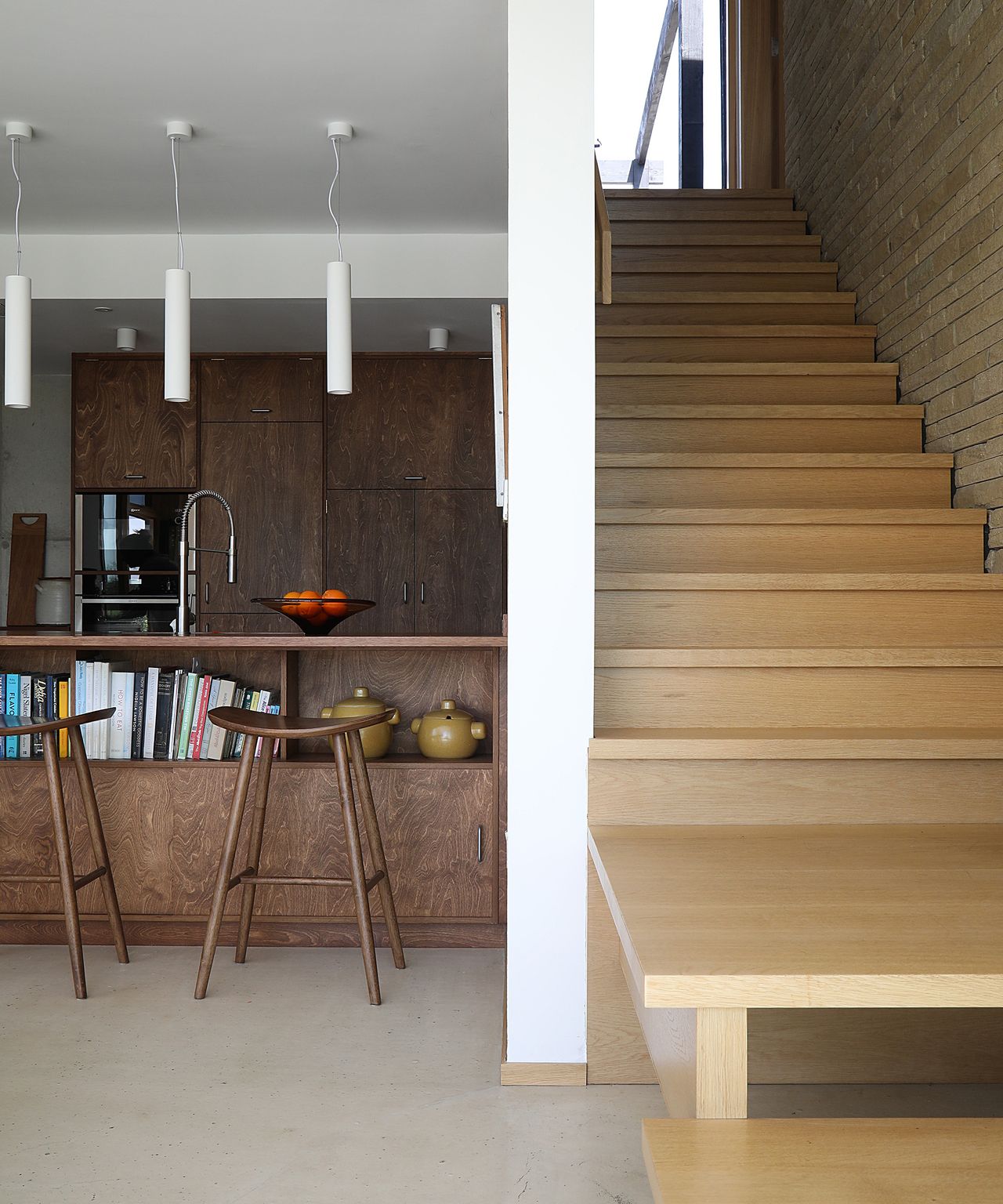 A light wooden staircase to the right of a kitchen which leads up to a second storey of a self build home