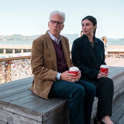 Ted Danson as Charles and Lilah Richcreek Estrada as Julie, holding take-out coffees while sitting on a wooden bench in front of the love locks, with San Francisco's Golden Gate Bridge in the background, in episode 101 of 'A Man on the Inside.'