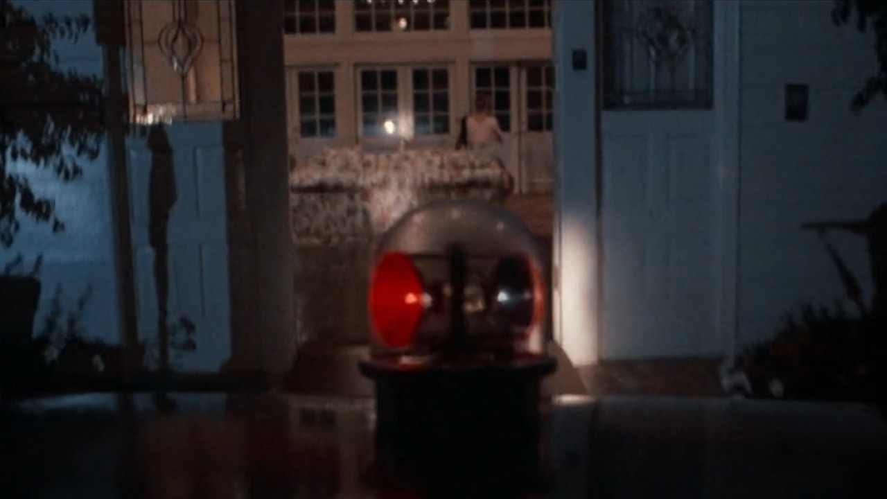 The top of a police car with a red siren facing into a house.
