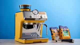 the de'longhi la specialista arte evo special edition truestart edition, with yellow body, showing the espresso machine attachments like tamper, tamping collar, grinder, and control buttons